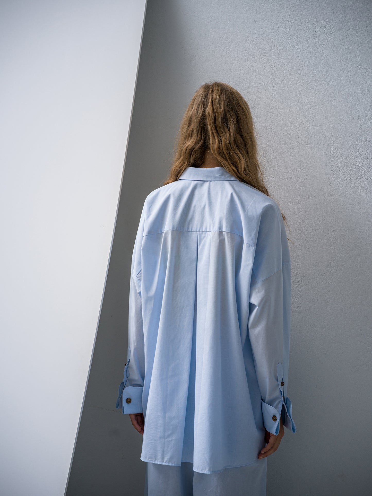 Person wearing a light blue shirt against a white wall