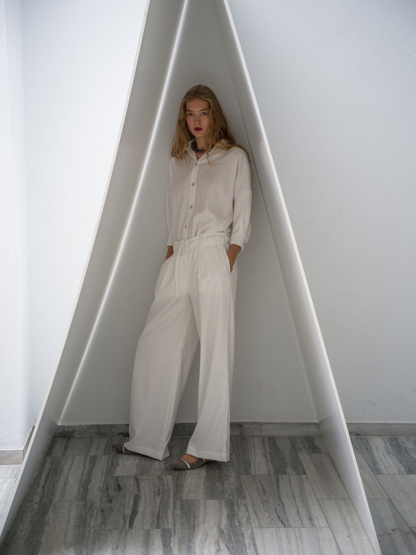 Person wearing a white outfit standing inside a geometrically shaped room.